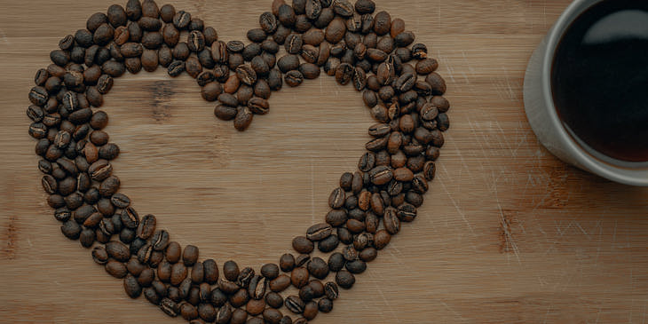 Corazón formado con granos de café sobre una superficie de madera con una taza de café negro al lado en un negocio de café ecuatoguineano.