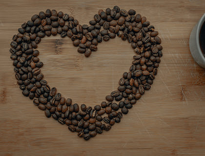 Corazón formado con granos de café sobre una superficie de madera con una taza de café negro al lado en un negocio de café ecuatoguineano.