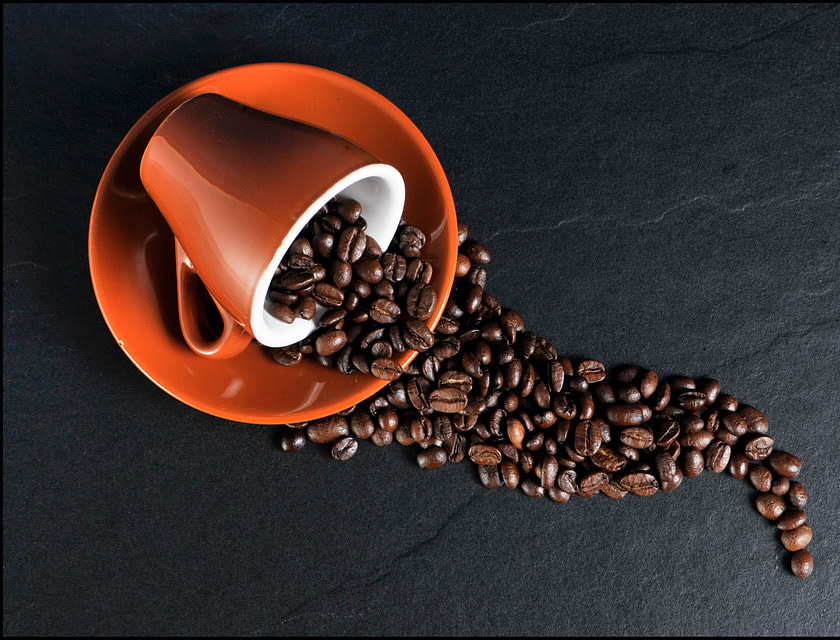 Taza color naranja acostada sobre un plato del mismo color con granos de café derramados sobre una superficie de piedra oscura en un negocio de café hondureño.