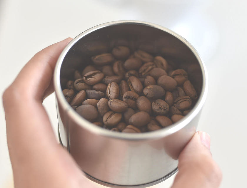 mano de mujer sosteniendo un recipiente con café colombiano en su interior sobre un fondo blanco