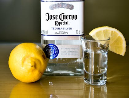 Botella de José Cuervo y un vaso con tequila y una rodaja de limón en una mesa de madera en un negocio de cata de tequila.