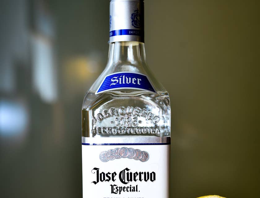 botella de José Cuervo y un vaso con tequila y una rodaja de limón en una mesa de madera en un negocio de cata de tequila