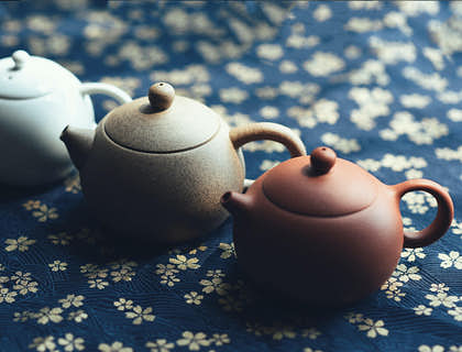 Teteras de cerámica de distintos colores sobre un mantel azul con flores blancas en un negocio de cerámica de Areguá