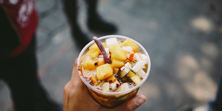 A hand holding a plastic cup with jicama, mango, chili powder, and chamoy for sale by a chamoy business.