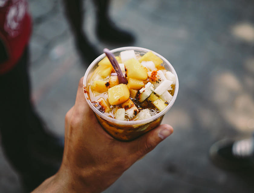 Una mano sosteniendo un vaso con jícama y mango con chile en polvo y chamoy en un negocio de chamoy