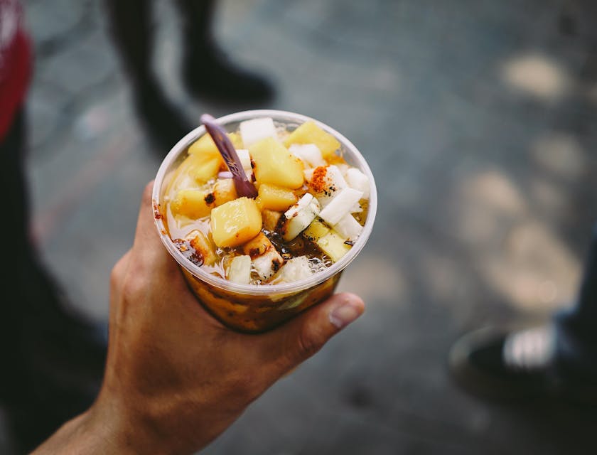 Una mano sosteniendo un vaso con jícama y mango con chile en polvo y chamoy en un negocio de chamoy