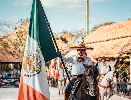 Un charro montando en un caballo con la bandera de México en un negocio de charrería.