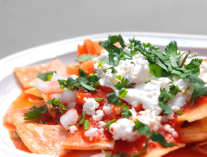 Chilaquiles rojos con queso y cilantro en un plato blanco en un negocio de chilaquiles