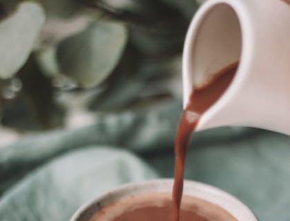 Una persona sirviendo chocolate caliente desde una chocolatera a una taza blanca en un negocio de chocolatera.