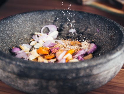 Mano esparciendo sal a un plato sobre una mesa de madera en un negocio de comida