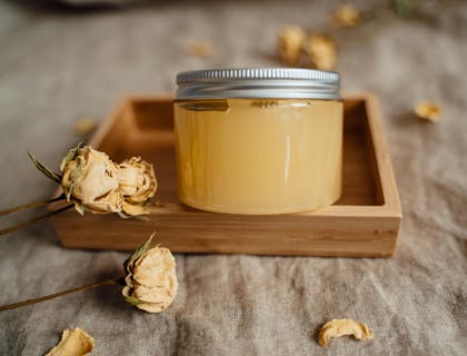 Un envase con crema de miel en una superficie de madera con flores marchitas de adorno en un negocio de cremas naturales.