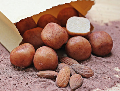 Bolitas de mazapán cubiertas de chocolate saliendo de una bolsa café y sobre polvo de cacao en un negocio de dulce de mazapán.
