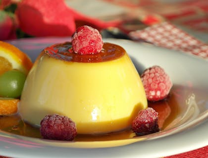 Un plato con flan acompañado de frutos rojos y una rodaja de naranja en un negocio de flan.