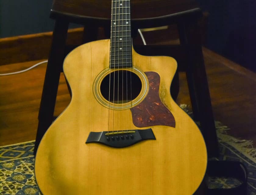 guitarra acústica de color café recargada en una silla de madera sobre un tapete en un suelo de madera con un fondo de pared azul oscuro en un negocio de guitarras