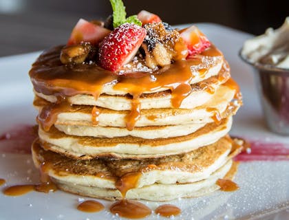 Un plato con hot cakes con cajeta, frutos rojos y crema batida en un negocio de hot cakes.