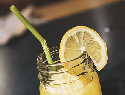 Un mason jar con limonada, hielo, una pajilla y una rodaja de limón en un negocio de limonadas.