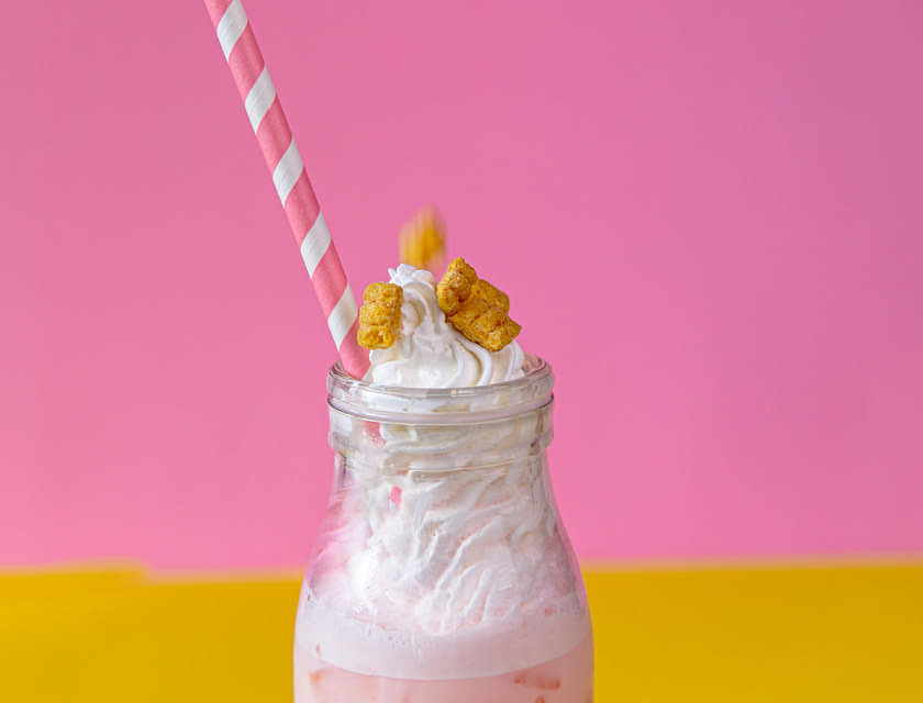Una malteada de fresa con crema batida encima y trozos de galleta frente a un fondo rosa y amarillo en un negocio de malteadas.