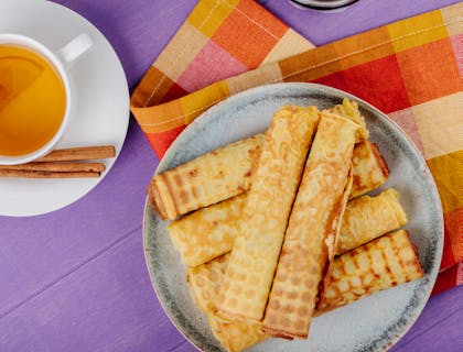 Marquesitas sobre plato gris en fondo morado junto a una taza de té de canela en un negocio de marquesitas