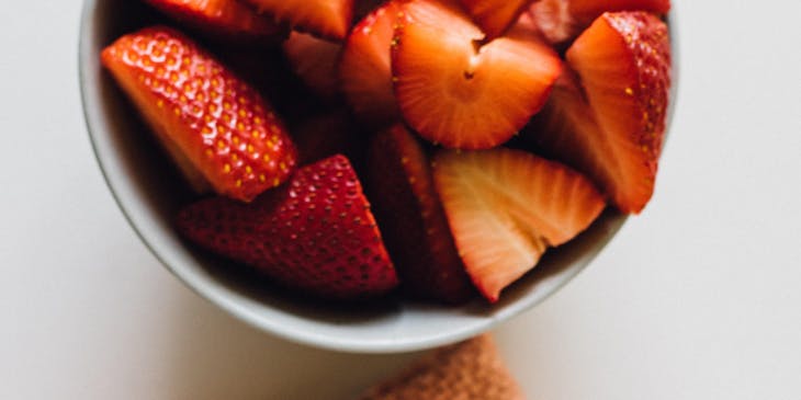 Una botella de masato fermentado junto a un bowl con fresas cortadas en un negocio de masato
