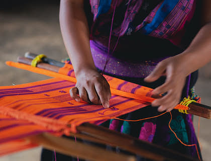 Una mujer tejiendo una mochila en un negocio de mochilas wayúus.