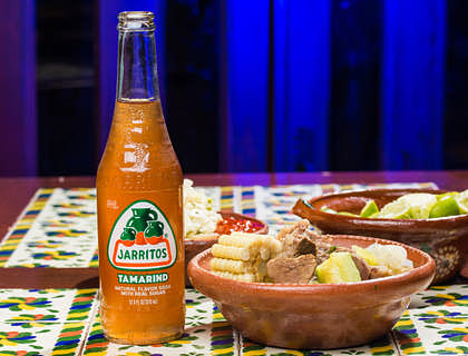Mondongo en una cazuela de cerámica a un lado de un refresco de naranja de jarritos en un negocio de mondongo.