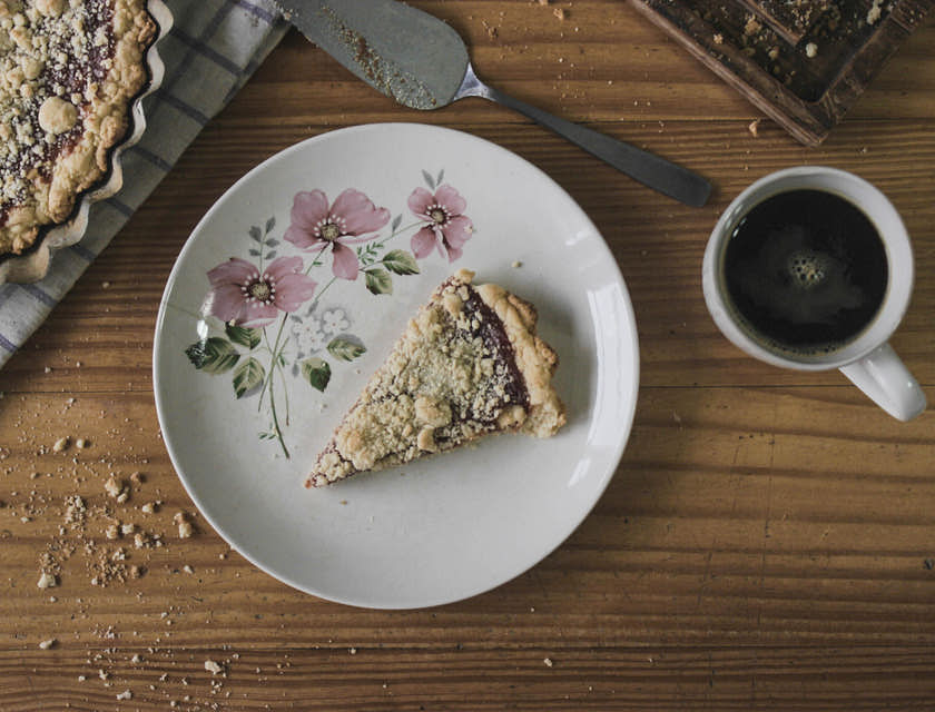 una rebanada de pastafrola sobre un plato de cerámica blanco a un lado de una pastafrola entera sobre una mesa de madera en un negocio de pastafrola