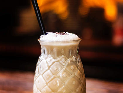 Vaso en forma de piña servido con piña colada y un popote sobre una base de madera en un negocio de piña colada.