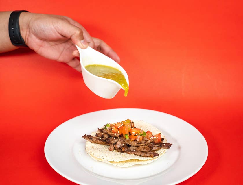 Salsa de pipián siendo vertida en un taco de carne en tortilla doble en un plato blanco en un negocio de pipián.