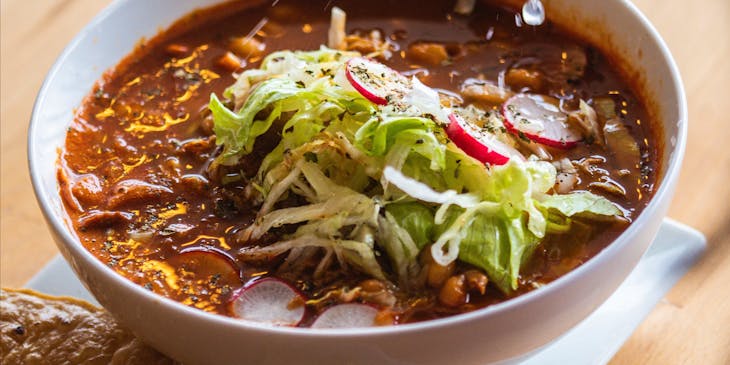 Mano femenina exprimiendo un limón sobre un plato de pozole.