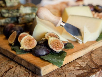 Higos en rodajas gruesas a un lado de cortes de queso sardo sobre una tabla de madera en un negocio de queso sardo.