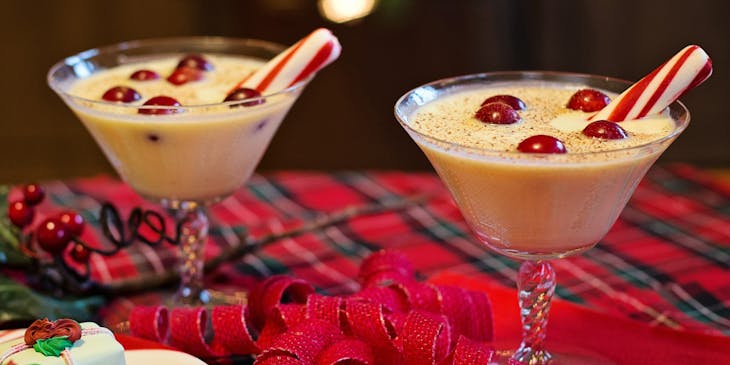 Dos copas con rompope de coco con adornos de dulces sobre una mesa con motivos navideños en un negocio de rompope.