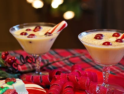 Dos copas con rompope de coco con adornos de dulces sobre una mesa con motivos navideños en un negocio de rompope.