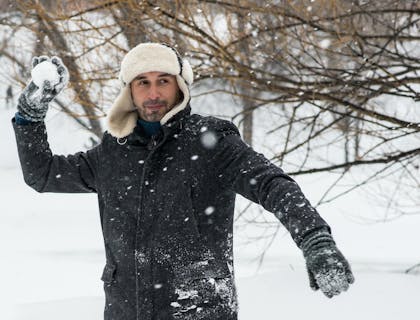 Un hombre lanzando una bola de nieve afuera de un negocio de ropa para invierno