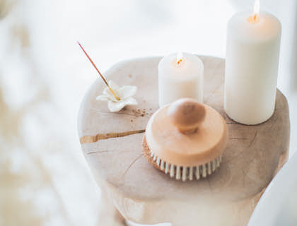 Un incienso encedido, velas blancas y una flor sobre un taburete en un negocio de sahumerios e incienso.