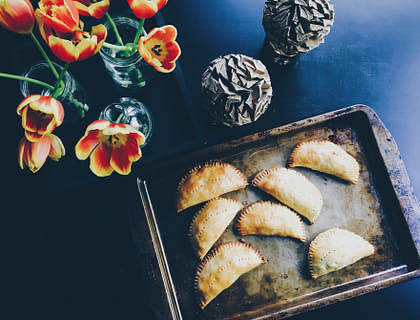 Una mesa con flores y piñas de pino a un lado de una charola con salteñas en un negocio de salteñas bolivianas.