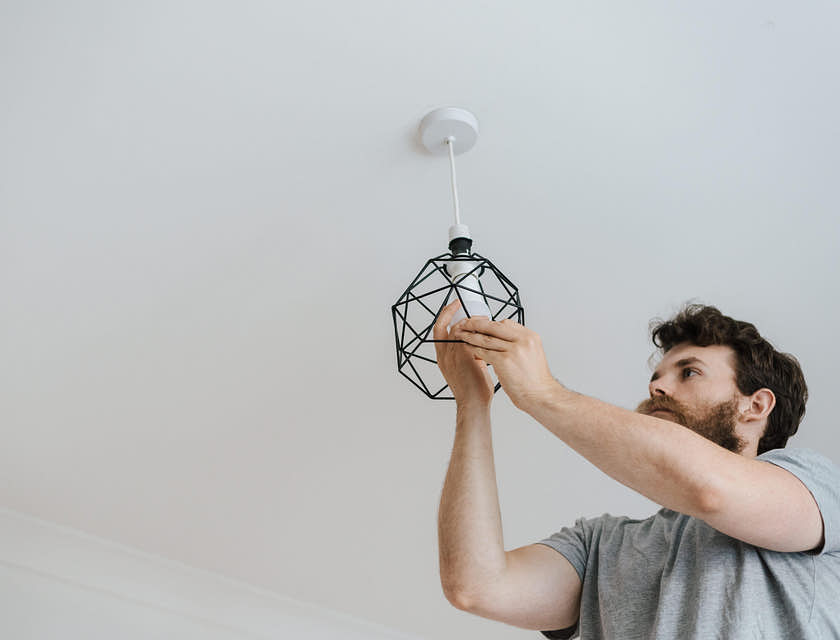 Um homem fazendo um serviço residencial instalando um lustre.