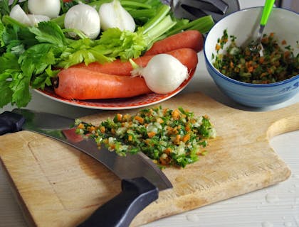 Una tabla de madera con sofrito recién hecho a un lado de un bowl lleno de sofrito en un negocio de sofrito.