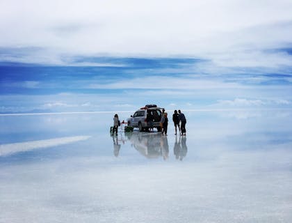 Vista del gran Salar de Uyuni con turistas de un negocio de tours a Uyuni en una camioneta y el efecto espejo en el suelo.
