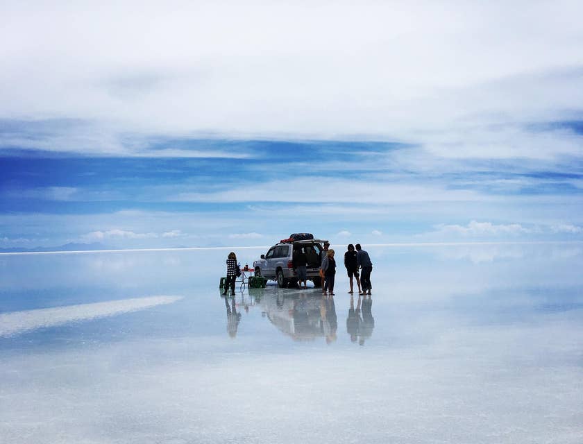 Vista del gran Salar de Uyuni con turistas de un negocio de tours a Uyuni en una camioneta y el efecto espejo en el suelo.