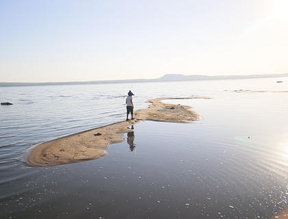 Mujer caminando con una caña de pescar sobre un estrecho de tierra en medio del lago Ypacaraí en un negocio de tours al Lago Ypacaraí.