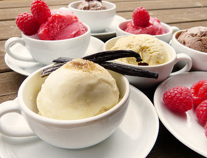 Tasas y platos blancos servidos con helado de vainilla y frutos rojos y dos vainas de vainilla encima sobre una base de madera en un negocio de vainilla.