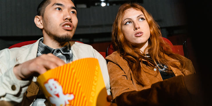 La imagen de una pareja sentada en las butacas de un cine con palomitas viendo una película.