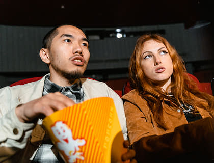 La imagen de una pareja sentada en las butacas de un cine con palomitas viendo una película.