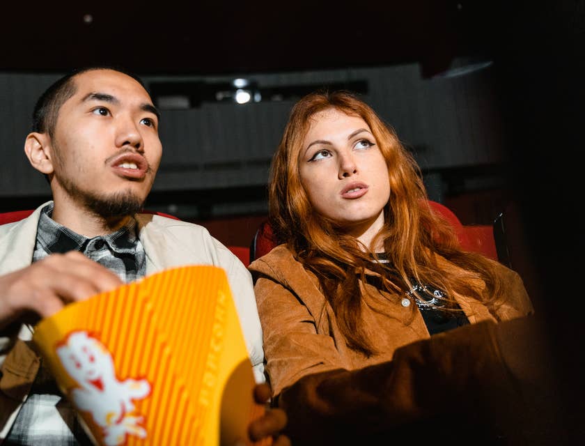La imagen de una pareja sentada en las butacas de un cine con palomitas viendo una película.