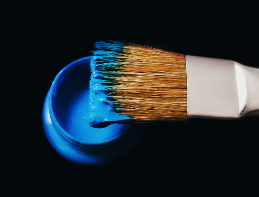 Una brocha sobre un bote de pintura azul sobre el fondo negro de una pinturería.