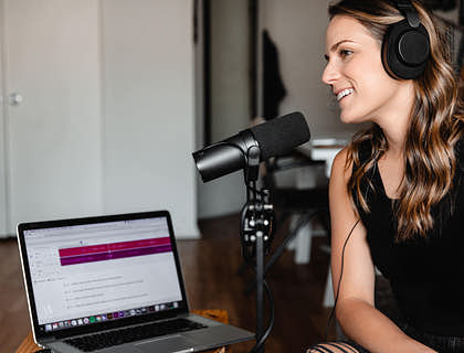 Una mujer con audífonos y un micrófono en una sala grabando un podcast en su computadora.