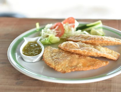 Un plato con tres pescadillas, ensalada y salsa sobre una mesa de madera en un puesto de pescadillas.