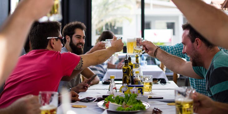 Hombres brindando con cerveza en interior de un restaurante asturiano.