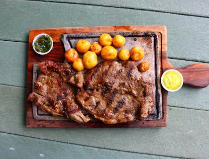 Plato de parrillada con dos vasos de aderezo sobre una superficie de madera en un restaurante colombiano.