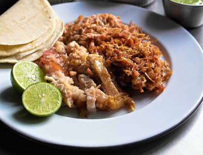 Un plato servido con carnitas tortillas y limón acompañadas de 3 salseros con cebolla cilantro y salsa verde en un restaurante de carnitas.